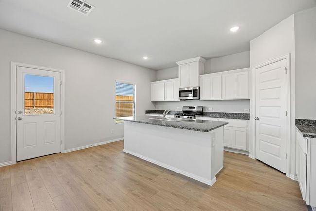 Kitchen featuring stainless steel appliances, light wood finished floors, a center island with sink, white cabinetry, and recessed lighting | Image 6