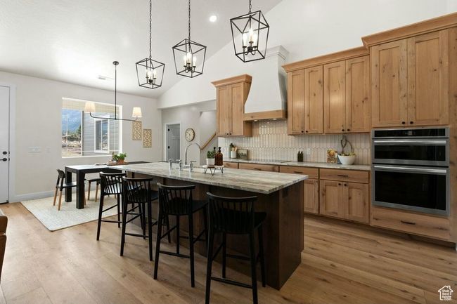 Kitchen featuring an island with sink, stainless steel double oven, decorative backsplash, a chandelier, and light wood-style flooring | Image 9