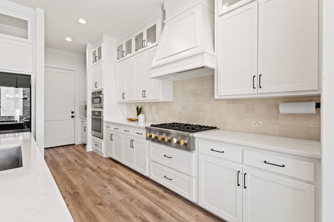 Kitchen with appliances with stainless steel finishes, custom range hood, white cabinets, tasteful backsplash, and recessed lighting | Image 7