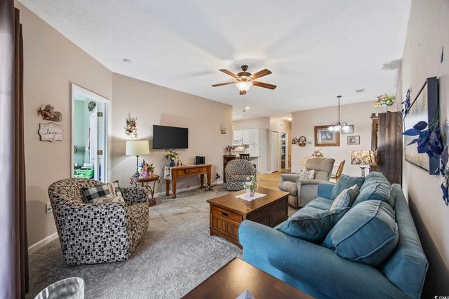 Carpeted living room with a chandelier, ceiling fan, and baseboards | Image 13
