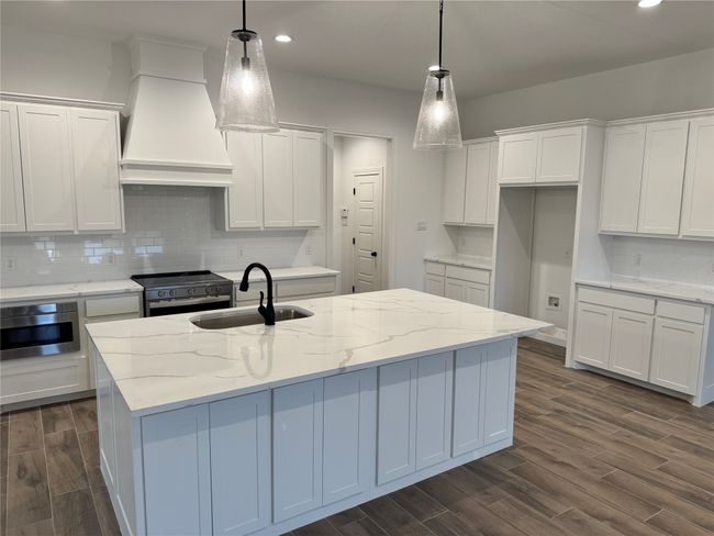 Kitchen with hanging light fixtures, sink, range with electric stovetop, and a kitchen island with sink | Image 4