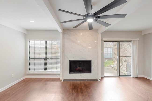 Unfurnished living room with wood finished floors, beamed ceiling, a high end fireplace, ceiling fan, and baseboards | Image 10