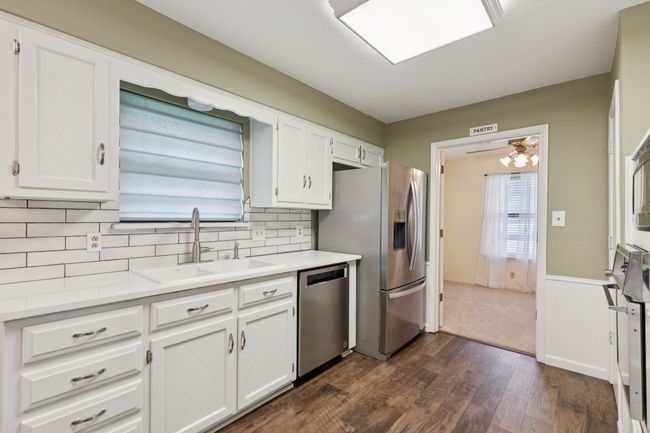 Kitchen featuring appliances with stainless steel finishes, white cabinetry, dark wood finished floors, light countertops, and decorative backsplash | Image 10
