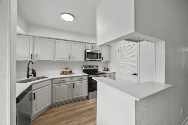 Kitchen featuring stainless steel appliances, light wood-type flooring, light countertops, backsplash, and a peninsula | Image 20