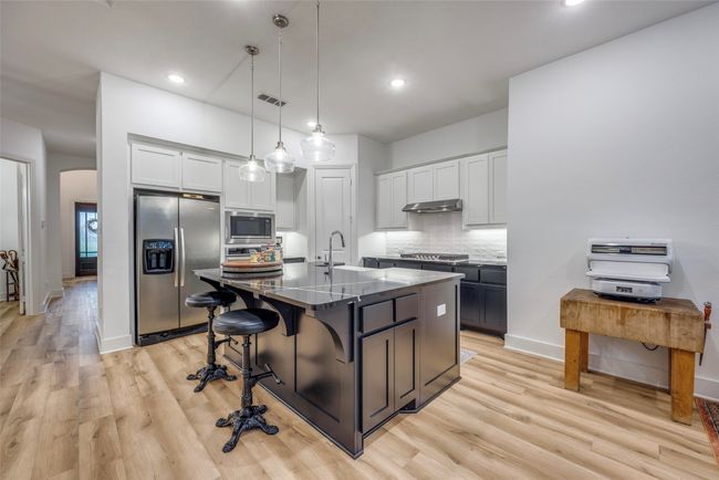 Kitchen with tasteful backsplash, visible vents, appliances with stainless steel finishes, under cabinet range hood, and a breakfast bar area | Image 8