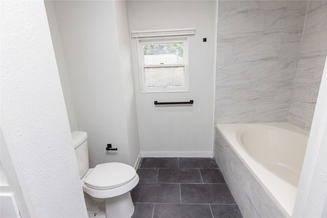 Bathroom with a bathtub, toilet, tile patterned floors, and baseboards | Image 26