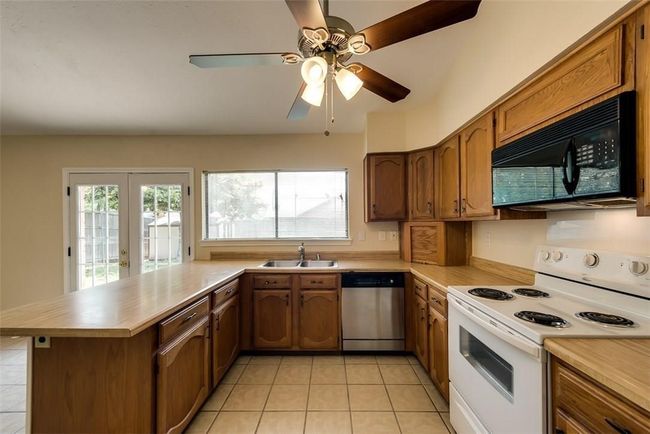 Kitchen featuring black microwave, stainless steel dishwasher, white electric stove, a sink, and brown cabinets | Image 9