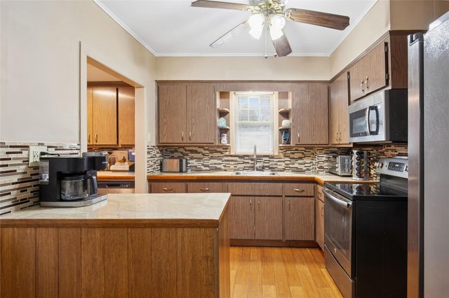 Kitchen with crown molding, a ceiling fan, open shelves, appliances with stainless steel finishes, and a sink | Image 9