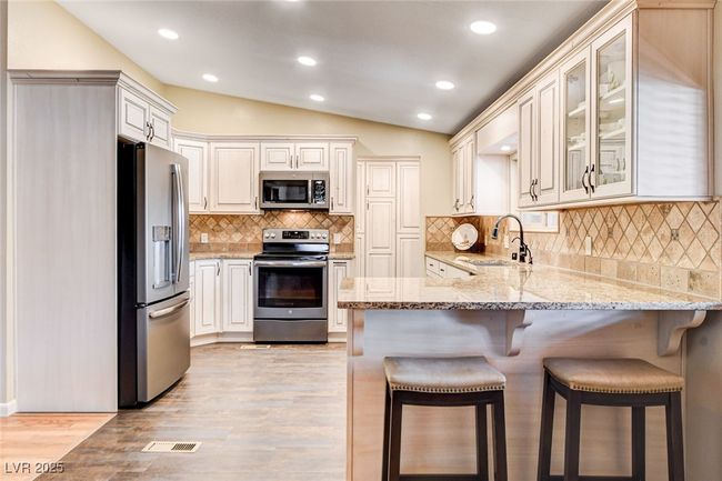 Kitchen with appliances with stainless steel finishes, a peninsula, light wood-type flooring, vaulted ceiling, and light stone countertops | Image 20