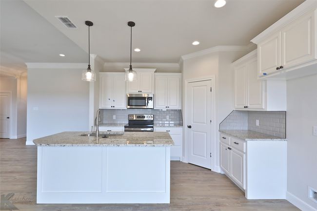 Kitchen with appliances with stainless steel finishes, crown molding, light stone counters, white cabinets, and tasteful backsplash | Image 9