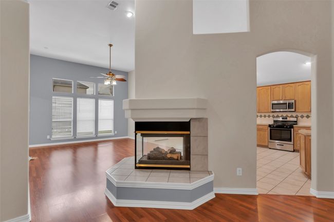 Unfurnished living room with arched walkways, ceiling fan, a multi sided fireplace, a high ceiling, and light wood-style flooring | Image 12