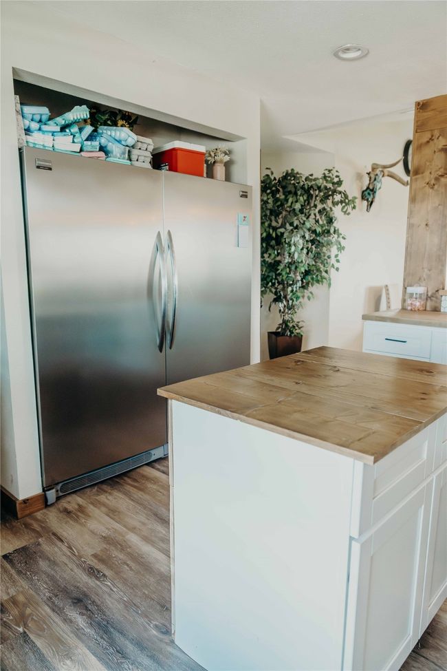 Kitchen with stainless steel refrigerator, butcher block counters, wood finished floors, white cabinetry, and recessed lighting | Image 11
