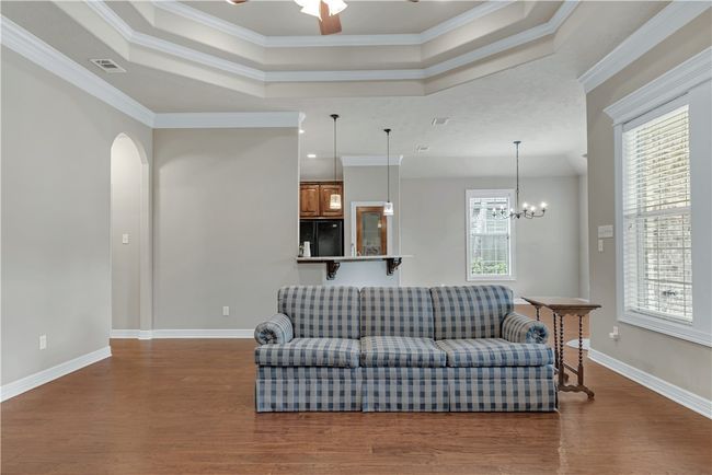 Living area with wood finished floors, a tray ceiling, ceiling fan, crown molding, and arched walkways | Image 9