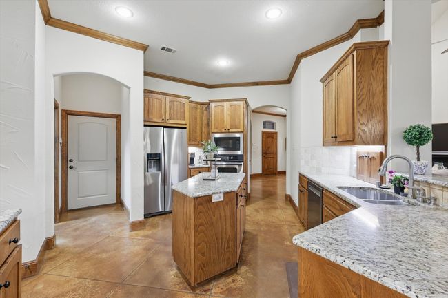 Kitchen featuring arched walkways, ornamental molding, light stone counters, backsplash, and appliances with stainless steel finishes | Image 14