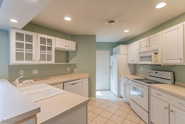 Kitchen featuring white appliances, recessed lighting, light tile patterned floors, white cabinetry, and light countertops | Image 10