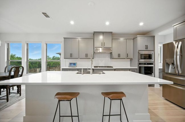 Kitchen featuring stainless steel appliances, gray cabinets, under cabinet range hood, a kitchen breakfast bar, and light countertops | Image 12