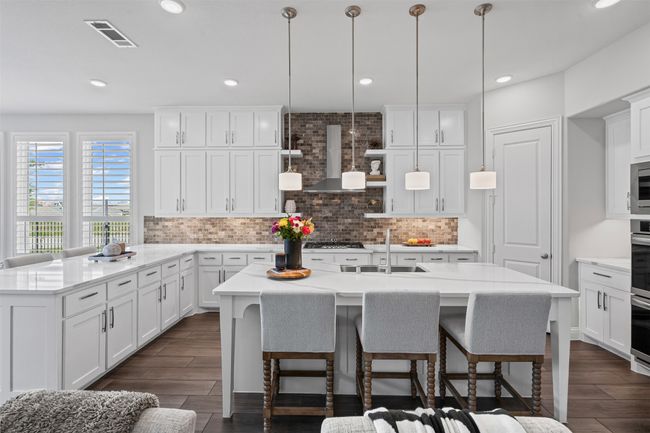 Kitchen featuring a sink, backsplash, a center island with sink, wall chimney exhaust hood, and a breakfast bar | Image 15