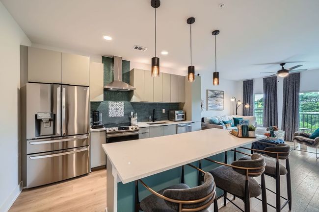 Kitchen featuring appliances with stainless steel finishes, wall chimney range hood, light wood finished floors, open floor plan, and a kitchen bar | Image 8