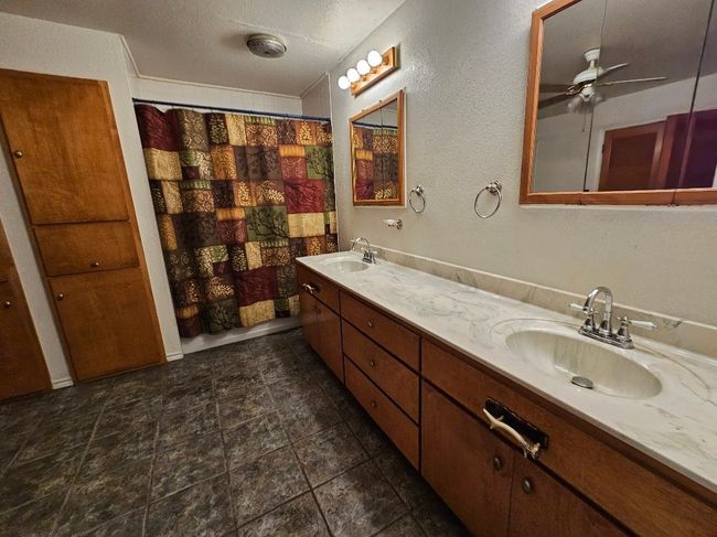 Bathroom with double vanity, a ceiling fan, a textured ceiling, a textured wall, and a shower with curtain | Image 14