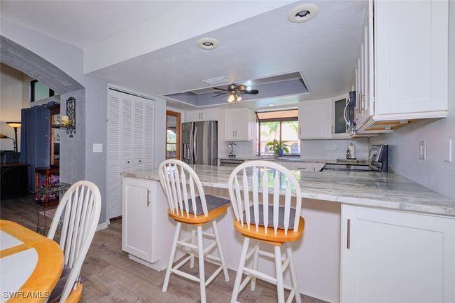 Kitchen featuring stainless steel refrigerator with ice dispenser, range, white cabinets, a peninsula, and light stone counters | Image 13