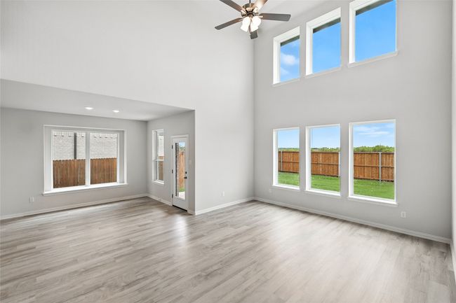 Unfurnished living room featuring a towering ceiling, wood finished floors, and ceiling fan | Image 14