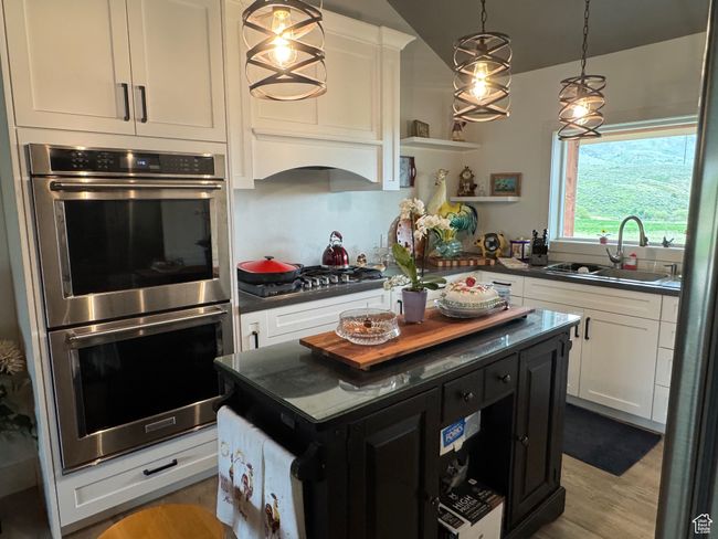 Kitchen with appliances with stainless steel finishes, a sink, dark countertops, white cabinetry, and lofted ceiling | Image 6