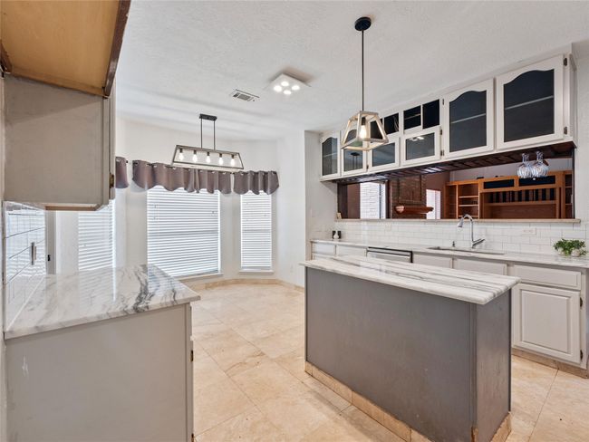 Kitchen with tasteful backsplash, glass insert cabinets, a center island, hanging light fixtures, and a textured ceiling | Image 9