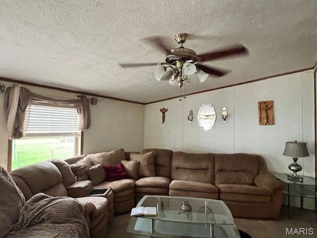 Carpeted living area with a textured ceiling, ceiling fan, and ornamental molding | Image 9