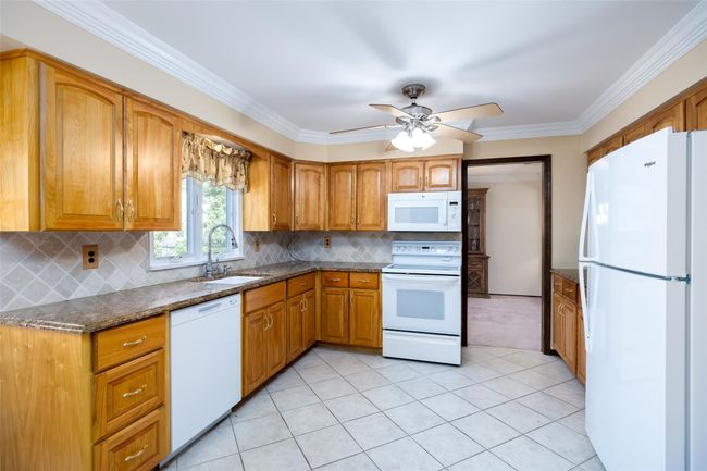 Kitchen with white appliances, brown cabinetry, and a sink | Image 15