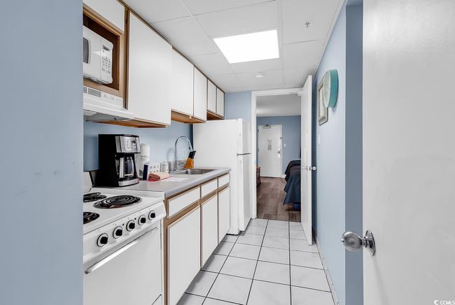 Kitchen with white appliances, white cabinets, light countertops, light tile patterned floors, and a paneled ceiling | Image 11