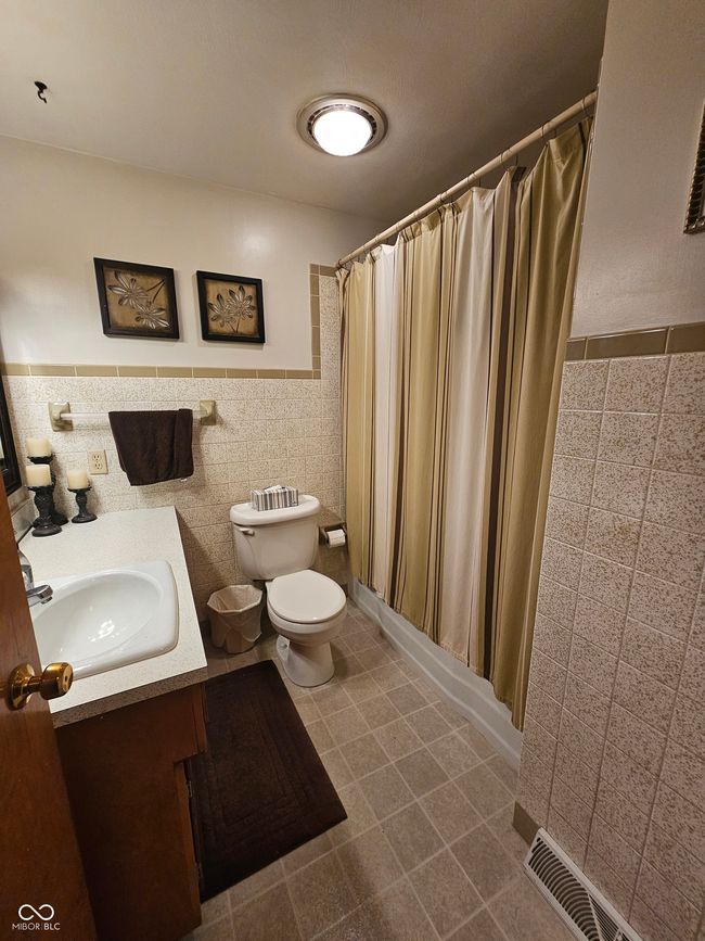 full bathroom featuring tile walls, vanity, a shower with curtain, and a wainscoted wall | Image 22