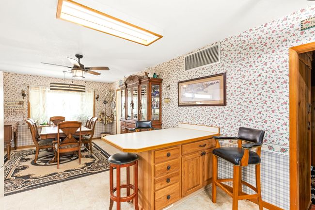 Kitchen featuring light countertops, a peninsula, wallpapered walls, a ceiling fan, and a kitchen breakfast bar | Image 45