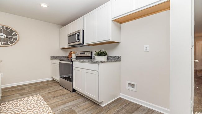 Kitchen with stainless steel appliances, dark stone countertops, white cabinets, and light wood-type flooring | Image 5