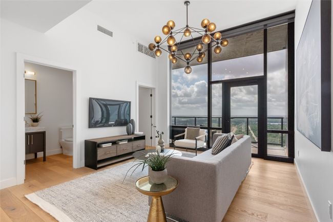 Living room with light wood finished floors, a chandelier, baseboards, and floor to ceiling windows | Image 22