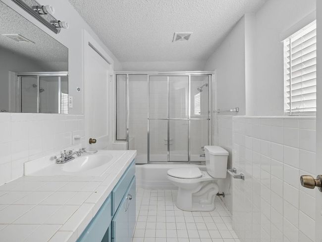 Full bath with tile walls, vanity, bath / shower combo with glass door, light tile patterned flooring, and a textured ceiling | Image 16