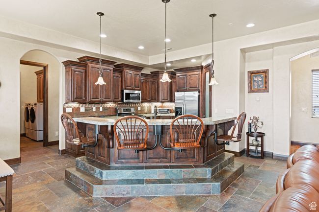Kitchen featuring appliances with stainless steel finishes, arched walkways, stone tile floors, washing machine and clothes dryer, and recessed lighting | Image 36
