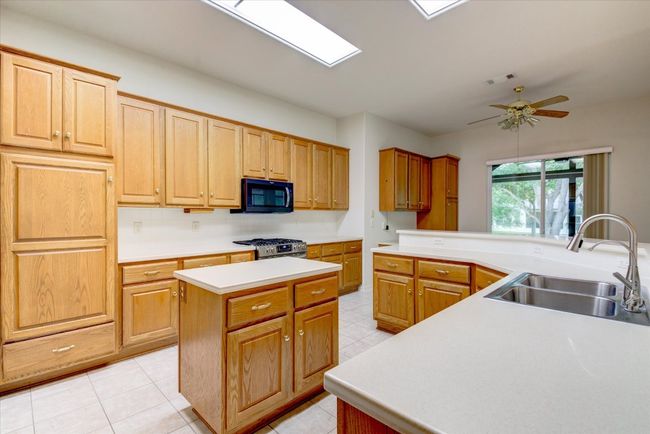 Kitchen featuring black microwave, stainless steel range with gas cooktop, a center island, a ceiling fan, and light countertops | Image 13