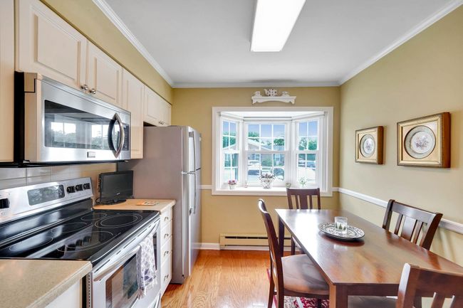 Kitchen featuring appliances with stainless steel finishes, a baseboard heating unit, decorative backsplash, light wood-style flooring, and white cabinets | Image 8
