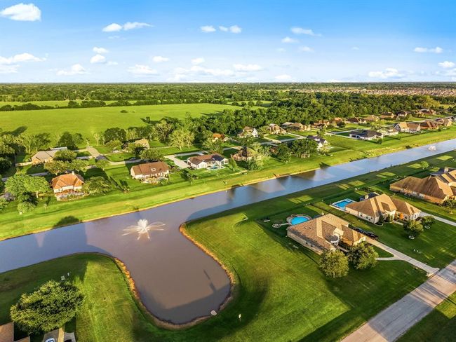 Experience peaceful living in a beautifully landscaped community with expansive green spaces and a scenic canal running through the neighborhood. This aerial view showcases the serene atmosphere, private waterfront lots, and a harmonious blend of nature and luxury living. | Image 44