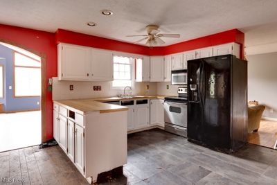 Kitchen featuring white cabinets, backsplash, stainless steel appliances, ceiling fan, and hardwood / wood-style flooring | Image 2