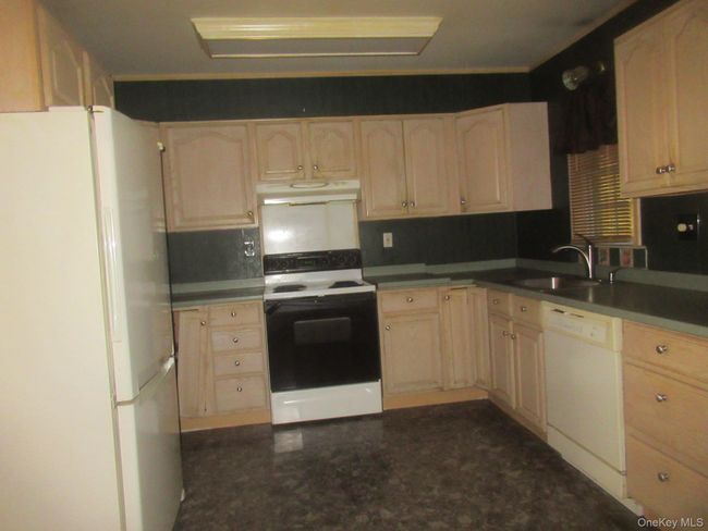 Kitchen featuring white appliances, under cabinet range hood, light brown cabinetry, and dark countertops | Image 11