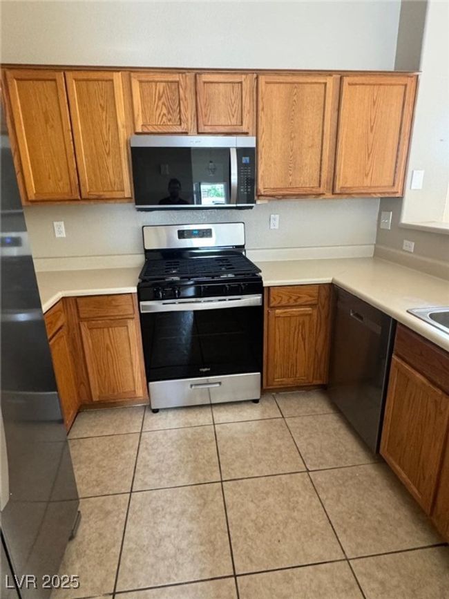 Kitchen featuring light countertops, light tile patterned floors, stainless steel appliances, and brown cabinets | Image 6
