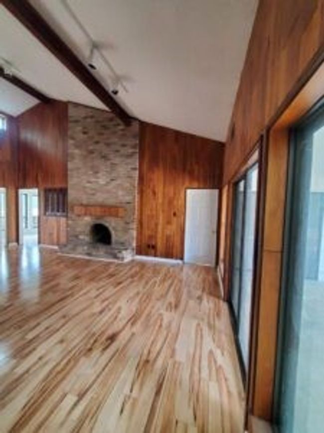 Unfurnished living room with wooden walls, wood finished floors, high vaulted ceiling, a fireplace, and beam ceiling | Image 10