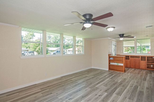 Unfurnished living room with ceiling fan, healthy amount of natural light, light wood-style flooring, a textured ceiling, and ornamental molding | Image 5