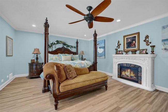 Bedroom with light wood finished floors, baseboards, recessed lighting, crown molding, and a glass covered fireplace | Image 23