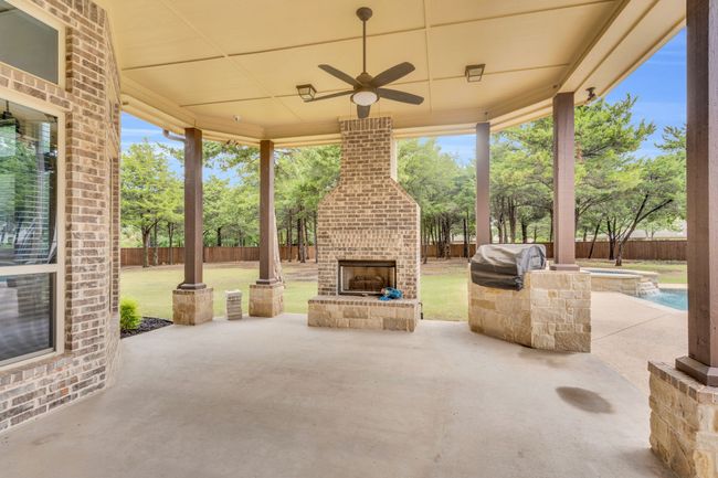 Fenced backyard featuring an outdoor brick fireplace, a patio area, a grill, ceiling fan, and a pool with connected hot tub | Image 35