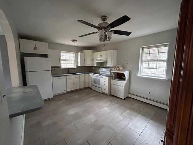 Kitchen with sink, white cabinets, white appliances, ceiling fan, and baseboard heating | Image 9
