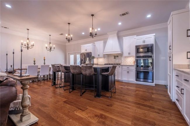 Kitchen featuring a breakfast bar, custom range hood, stainless steel appliances, white cabinetry, and an island with sink | Image 9