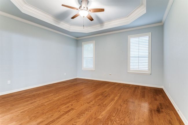Primary Bedroom with tray ceilings, wood floors lots of natural light, and plantation shutters. ornamental molding, and wood finished floors | Image 13
