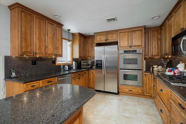 Kitchen with appliances with stainless steel finishes, brown cabinets, backsplash, light tile patterned floors, and recessed lighting | Image 7